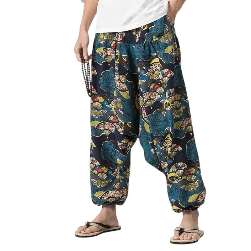 COMFORTH harem pants with a dark blue base and a repeating pattern of stylized fans in teal, yellow, and red. Loose fit, cuffed ankles.