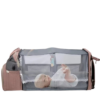 COMFORT diaper bag backpack with bassinet in pink and grey, featuring a mesh canopy and a baby resting inside.