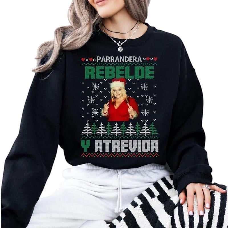 COMFORT black unisex graphic sweatshirt with "Parrandera Rebelde Y Atrevida" text, snowflakes, Christmas trees, and a woman giving the middle finger.