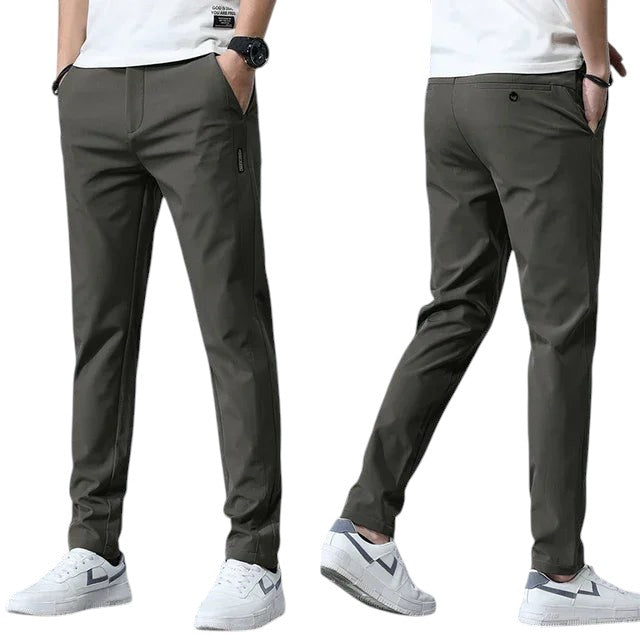 COMFORTH Men's slim-fit dark grey stretch chino pants with pockets and belt loops. Model wearing white t-shirt and sneakers.