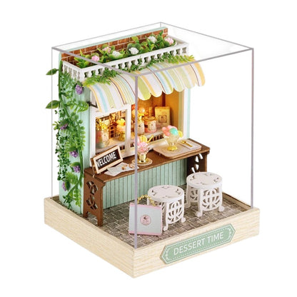 COMFORTH Miniature dollhouse bakery kit with ice cream, pastries, and seating. Features green vines, striped awning, and "Welcome" sign.