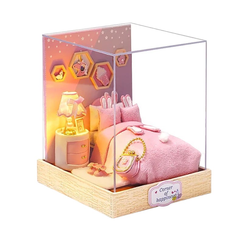 COMFORT miniature dollhouse building kit featuring a pink bedroom with a bed, nightstand, lamp, and wall decor. Includes bunny ear pillows.