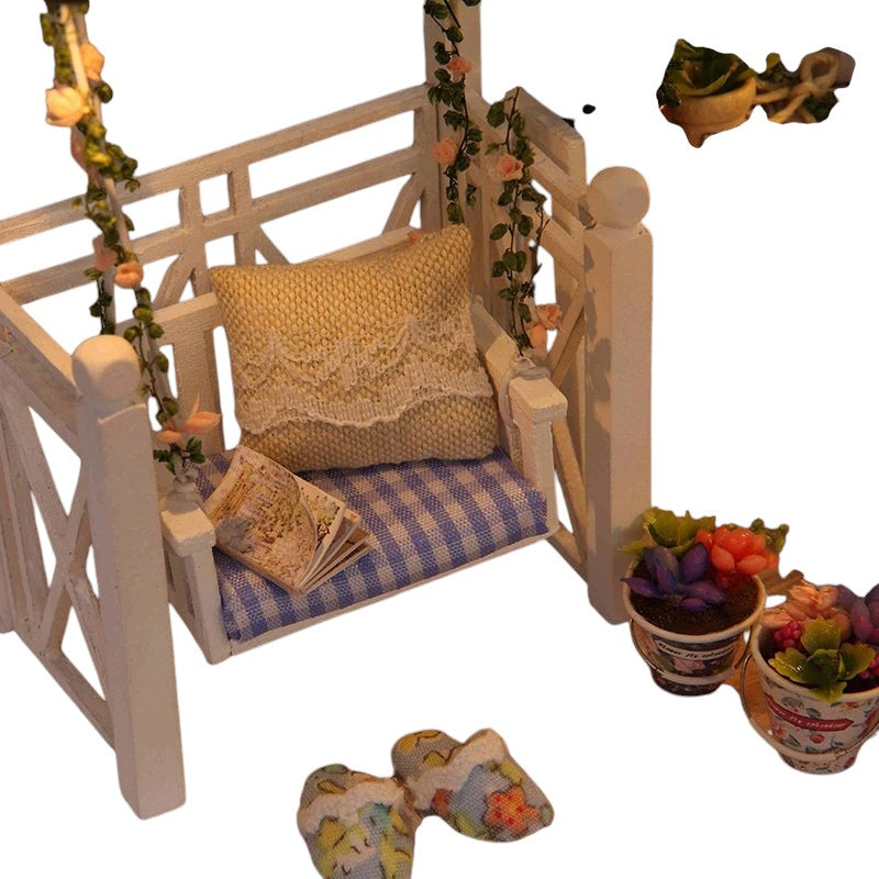 COMFORTH miniature dollhouse building kit with a white porch swing, blue gingham cushion, yellow pillow, and potted plants.