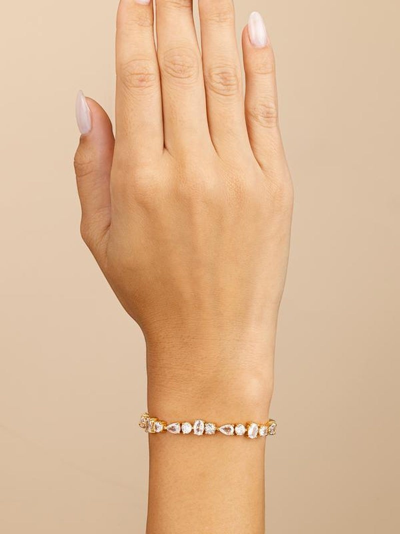 COMFORTH Mixed shape tennis bracelet with clear crystal accents on a gold-tone finish. Features round, oval, and pear cuts.
