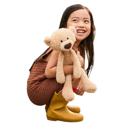 COMFORT plush teddy bear toy in beige, held by a smiling young girl wearing a brown dress and yellow boots.