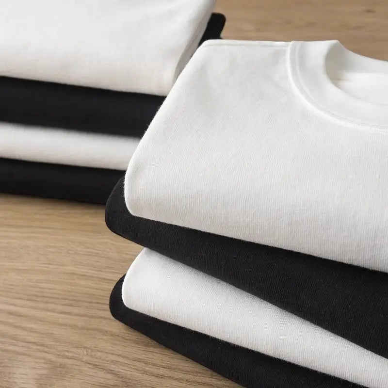 COMFORTH white crewneck t-shirt made of soft cotton, folded on top of black t-shirts.