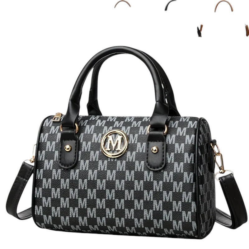 COMFORTH Monogram barrel handbag with shoulder strap, black and grey monogram print, gold M emblem, top handles, and detachable strap.